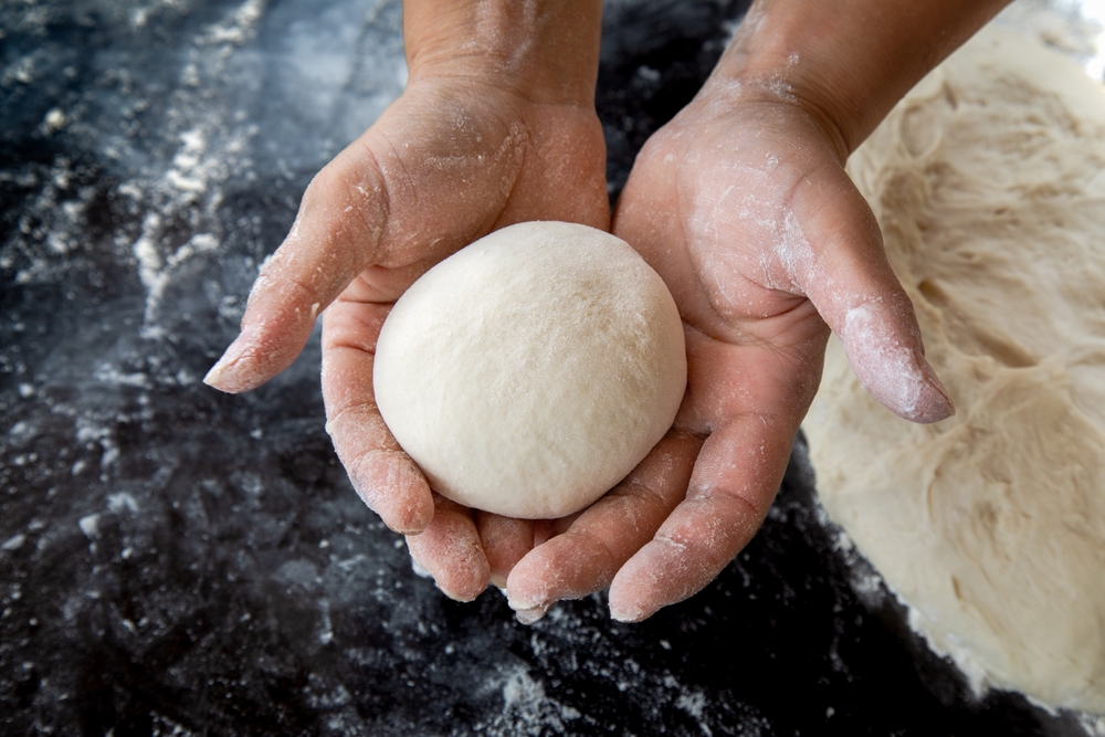 Person holding a rounded bread roll during a bread-making lesson