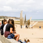 Students sitting on Omaha Beach next to famous war memorial
