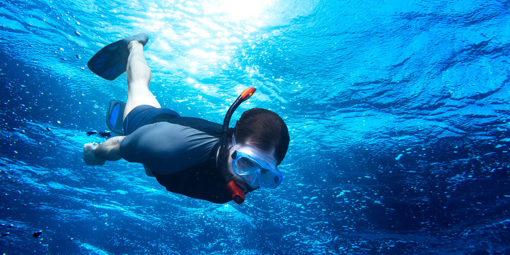 young man diving snorkeling down into the deep blue ocean sea against the sunlight