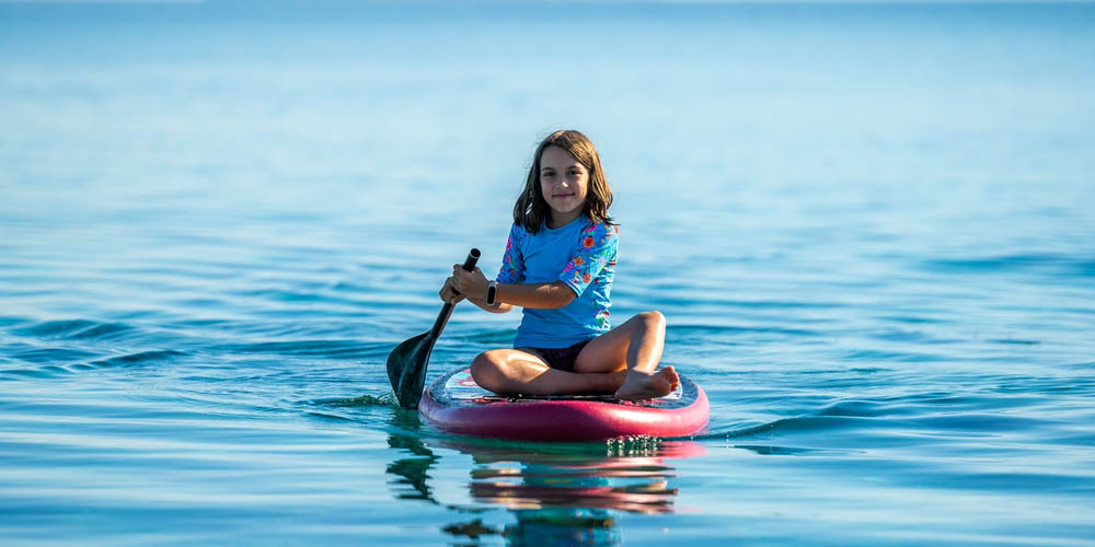 Young girl sitting on a stand up paddle board