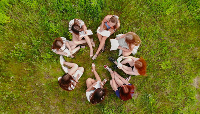 Teamwork concept. A group of female student girls are sitting on the grass and solving problems.
