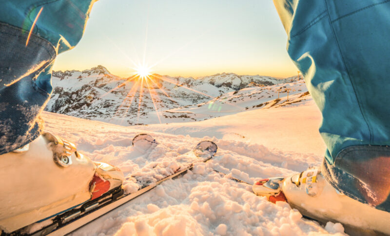 Close-up of a person's skis in the snow with the sun shining in the distance