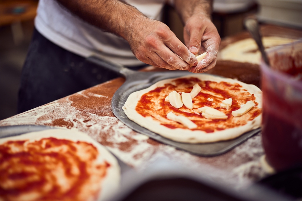 Close-up of a pizza maker, putting all the ingredients on the pizza dough.