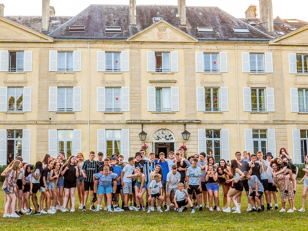 Group of students all posing and cheering outside the Chateau du Molay in Normandy