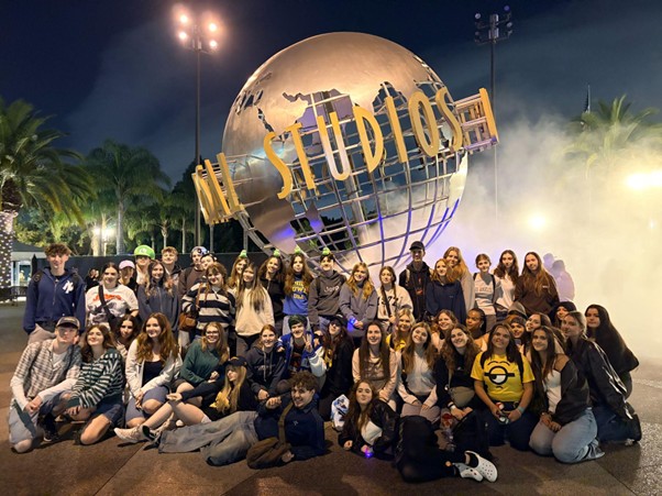 A large group of students stood around the Universal Studios Globe, smiling and looking at the camera. It is night time.
