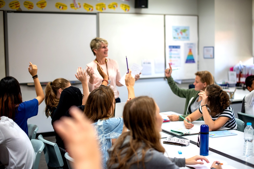 Students raising their hand to answer a teacher's question in a classroom