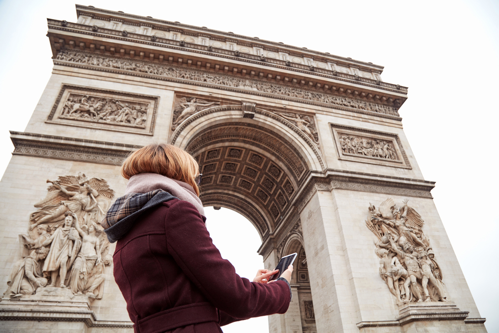 Student girl checking her mobile phone next to the Arc de Triomphe in Paris